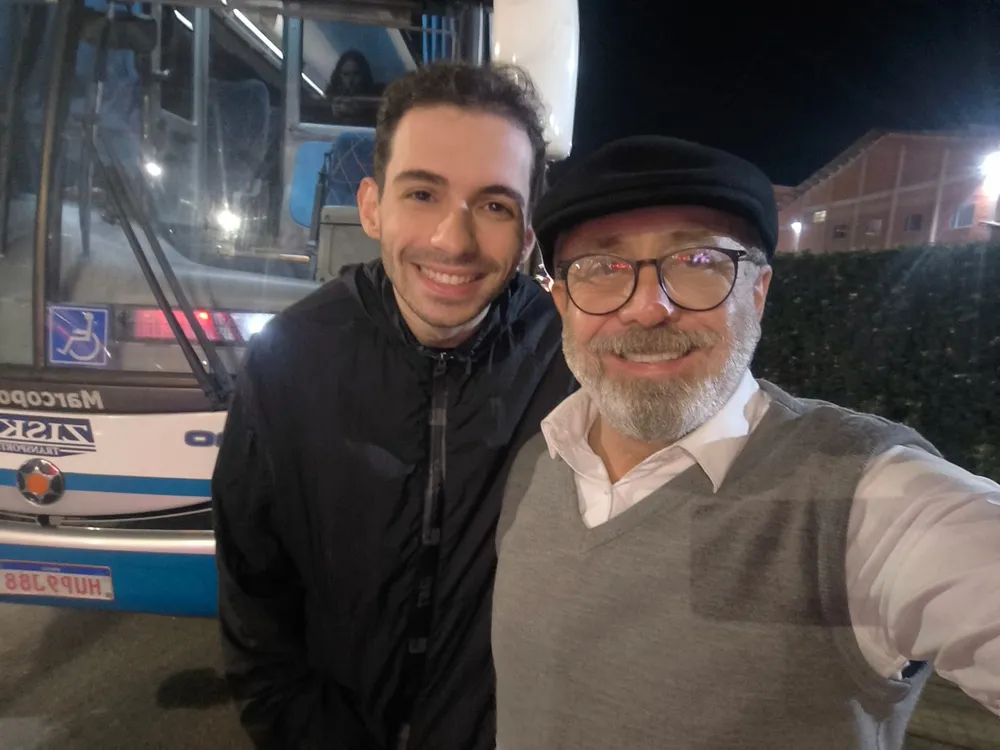 Sérgio com um passageiro na frente do ônibus, à noite